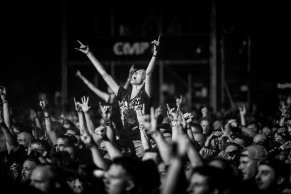 Begeisterte Festivalbesucher bei einem Metal-Konzert, mit erhobenen Armen und 'Metal-Handzeichen' inmitten einer Menschenmenge – ausgelassene Stimmung bei Nacht.